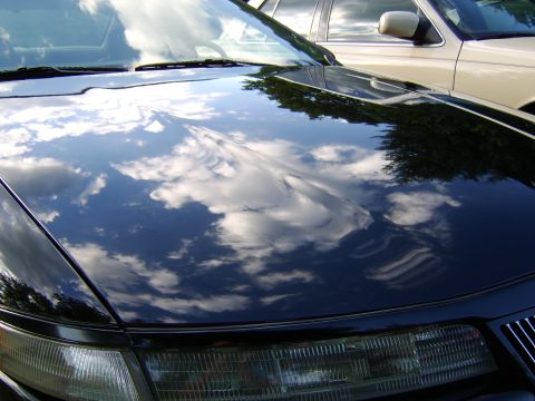 1996 Mercury Grand Marquis - Reflections of clouds on a black car's hood, with another vehicle partially visible in the background.
