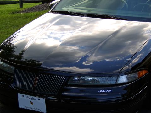 1996 Mercury Grand Marquis - Reflections on a black car hood show clouds and trees. The car has a Maryland license plate and 'LINCOLN' text.