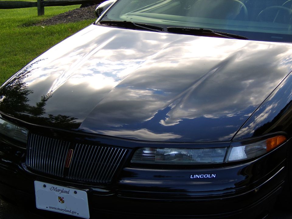 Glossy black front end with Lincoln-badged grille and headlights, clouds reflected in the polished hood