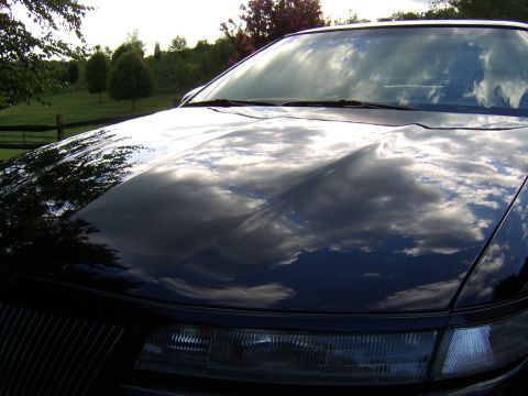 1996 Mercury Grand Marquis - The glossy hood of a dark-colored car reflects the sky and surrounding landscape.