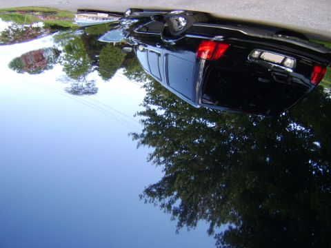 1996 Mercury Grand Marquis - A black sedan is viewed from the rear, with reflections of trees and the sky visible on its polished surface.