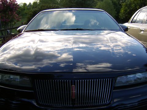 1996 Mercury Grand Marquis - Front view of a black car, showing the hood with cloud reflections and a chrome grille.