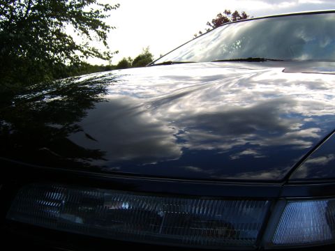 1996 Mercury Grand Marquis - Clouds and trees reflect on the hood of a dark-colored car.