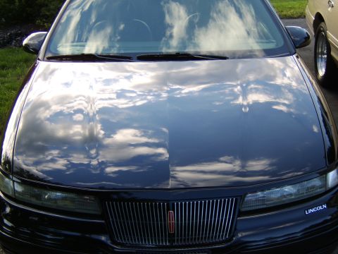 1996 Mercury Grand Marquis - Reflections of clouds on the hood of a black Lincoln Town Car. A portion of another vehicle is visible on the right.