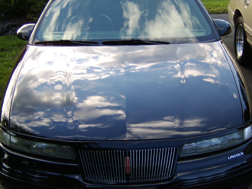 Glossy black hood and chrome waterfall grille with Lincoln badge, reflecting clouds