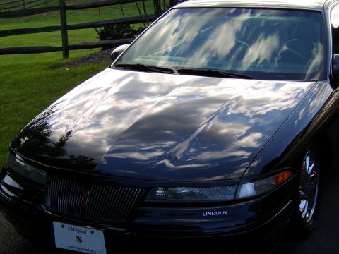 1996 Mercury Grand Marquis - The front of a black car is shown with the hood reflecting the sky and clouds.