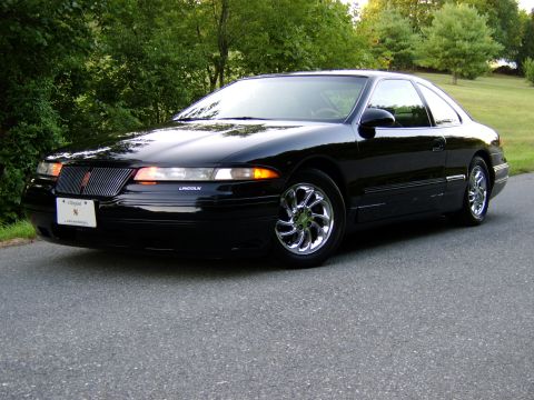 1996 Mercury Grand Marquis - A black Lincoln Mark VIII is parked on a paved road with trees in the background.