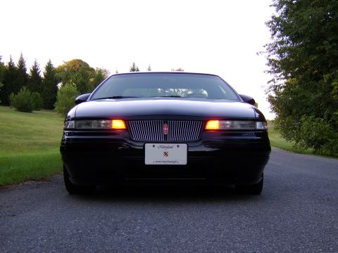 1996 Mercury Grand Marquis - A black Lincoln Mark VIII is shown from the front, parked on a paved road with trees and grass in the background.