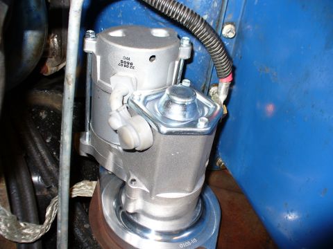1978 Ford Bronco - A freshly installed aluminum mini gear-reduction starter bolted to the bellhousing, viewed from below in the engine bay next to a blue-pain…