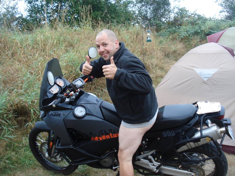Guy in underwear giving thumbs up on a KTM motorcycle at a campsite