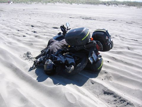 1979 Ford Bronco - Motorcycle tipped over in the sand with rider beside it on a beach.