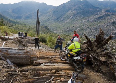 1979 Ford Bronco - Riders tackle a difficult mountain path, with multiple motorcycles and people visible amidst debris and a vast, treed landscape.
