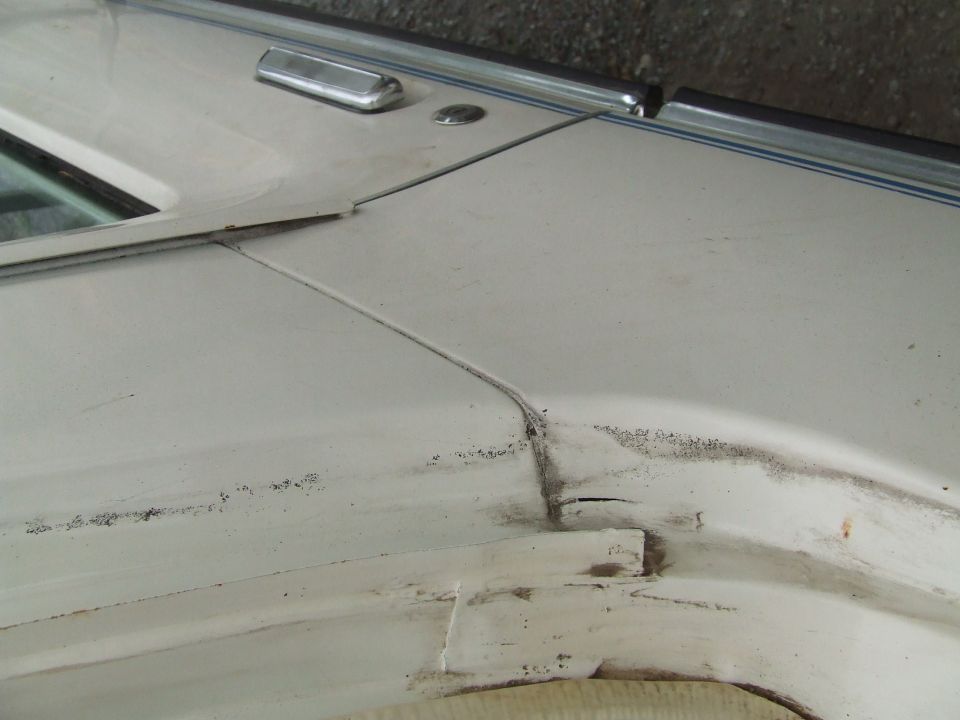 White vehicle door seam with chrome trim and visible damage