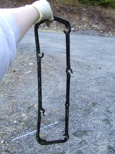 1979 Ford Bronco - A gloved hand holds a worn valve cover gasket outdoors on a gravel surface.