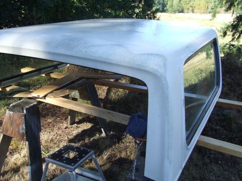 1979 Ford Bronco - A white pickup truck cap, possibly for a 1979 Ford Bronco, is shown disassembled and supported by sawhorses outdoors.