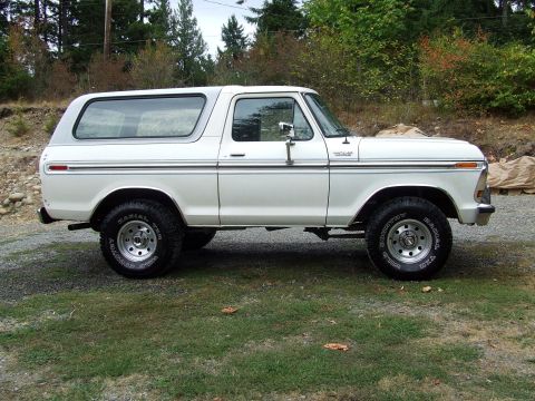 1979 Ford Bronco - White Ford Bronco parked on a gravel and grass area with trees in the background.