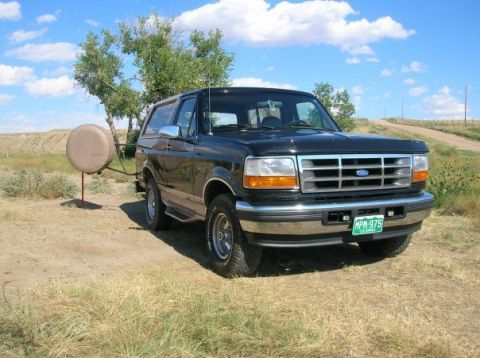 1996 Ford Bronco - A black 1996 Ford Bronco is parked outdoors on a dirt road under a blue sky with scattered clouds.