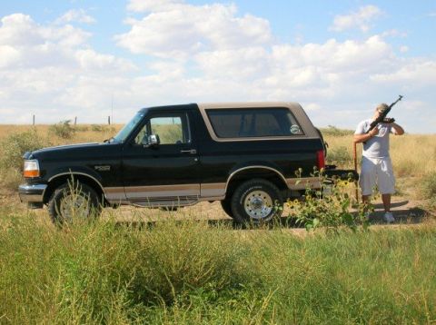 1996 Ford Bronco - A 1996 Ford Bronco is seen parked in a field with a man holding a rifle nearby.