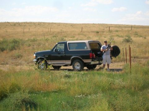 1996 Ford Bronco - Man with rifle stands by a 1996 Ford Bronco in a field.