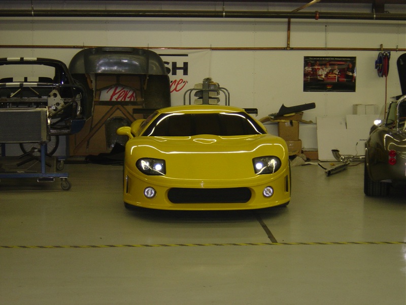 Yellow sports car front view in workshop, another car visible on the right