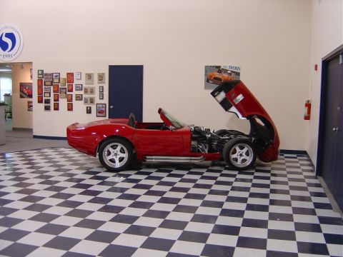 1996 Ford Bronco - A red convertible sports car is displayed with its hood open, revealing the engine, in a room with a checkered floor.