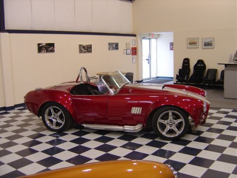 1996 Ford Bronco - A red convertible sports car with side pipes and racing stripes is parked indoors on a checkered floor.