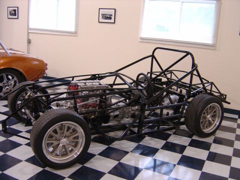 1996 Ford Bronco - A custom-built race car chassis is displayed indoors next to an orange vehicle.