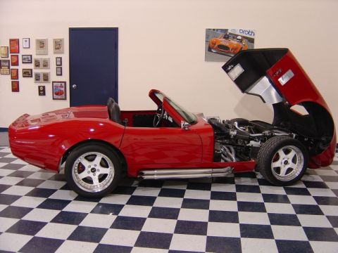 1996 Ford Bronco - A red convertible sports car is parked indoors with its hood open, displaying its engine and custom features.