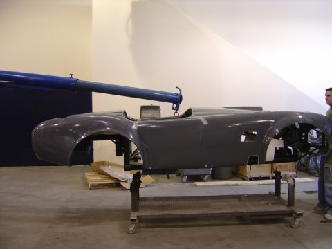 1996 Ford Bronco - A gray car body, likely a replica, is suspended by a crane in a workshop setting.