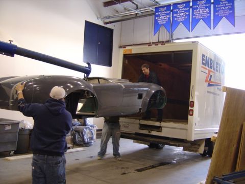 1996 Ford Bronco - Workers load a car body into a truck, with championship banners hanging overhead.