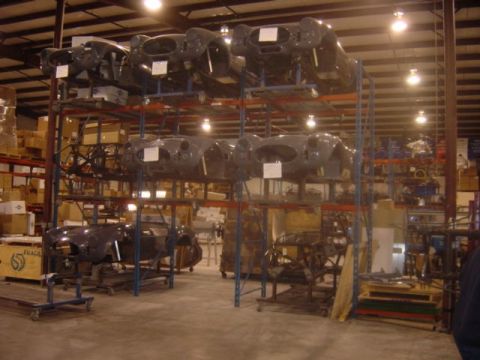 1996 Ford Bronco - Multiple car bodies are organized on shelving units within a large warehouse facility.