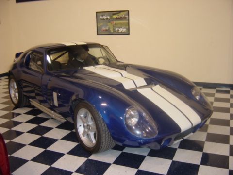 1996 Ford Bronco - A blue sports car with white racing stripes is parked inside a garage with a checkered floor.