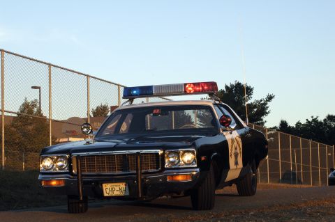 1973 Dodge 1500 - A 1973 Dodge 1500 police car is seen from the front, parked near a chain-link fence.