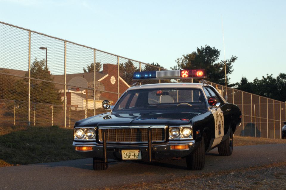 Black and white police car with light bar, front view. License plate reads CHP-NH
