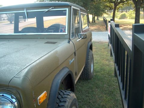 1979 Ford Bronco - This olive green 1978 Ford Bronco is seen from the front quarter, parked on grass beside a black fence.