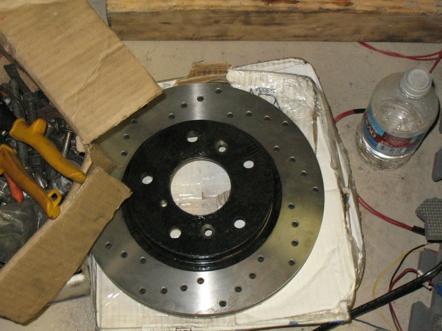 perforated brake rotor in cardboard packaging with tools and a water bottle nearby