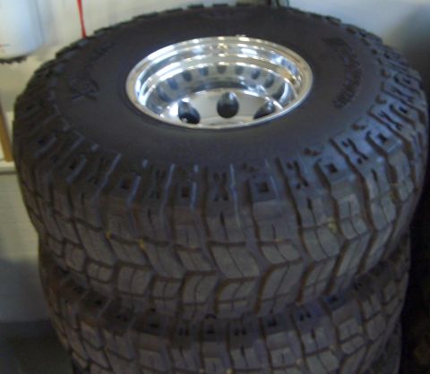 1974 Ford Bronco - Three off-road tires with chrome rims are stacked, showing aggressive tread patterns.