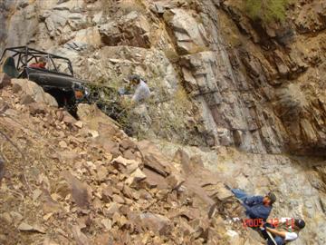 1994 Ford Bronco - Off-road vehicle struggles on a steep, rocky mountain trail with assistance from onlookers.