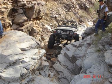 1994 Ford Bronco - A Jeep Wrangler tackles a challenging rocky terrain, with onlookers observing from the side.