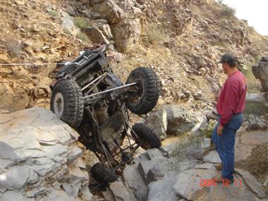 1994 Ford Bronco - An off-road vehicle is tilted on its side on a rocky incline, with a man observing the situation.