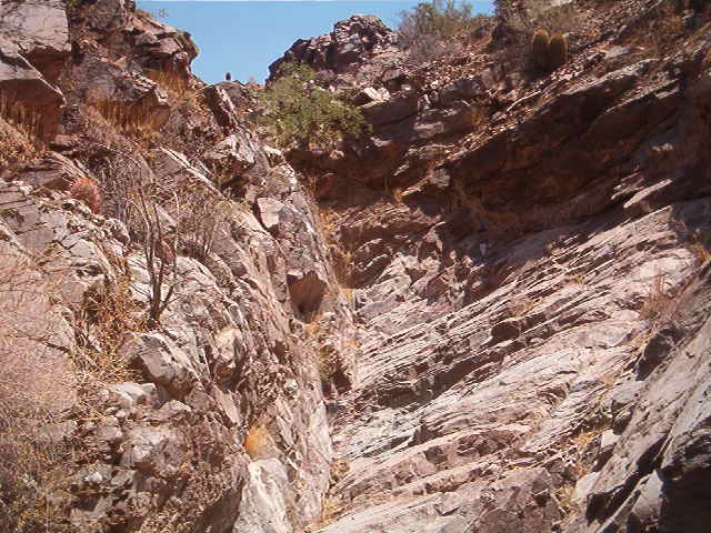 Rocky canyon with sparse vegetation under a clear blue sky. Watermark reads SUPERMOTORS