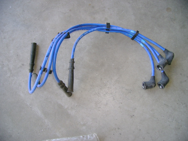 Set of blue spark plug wires with black boots on a concrete surface