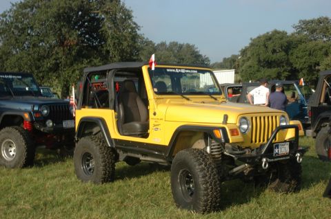 2001 Jeep Wrangler - A yellow Jeep Wrangler is parked on grass next to other Jeeps, with a website sticker on its windshield.