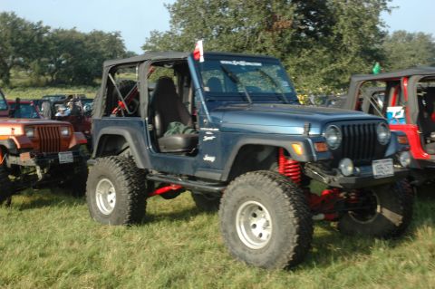 2001 Jeep Wrangler - Multiple modified Jeep Wranglers are parked on a grassy field under a clear sky.