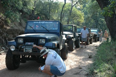 2001 Jeep Wrangler - A line of Jeep Wranglers on a dirt road, with people gathered around the lead vehicle.