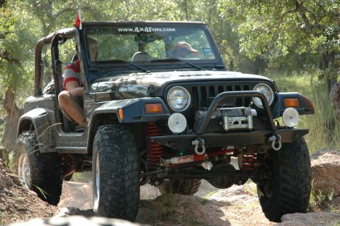 2001 Jeep Wrangler - This modified Jeep Wrangler is navigating a rocky, off-road trail surrounded by greenery.