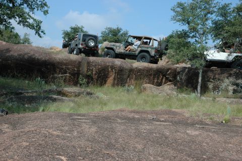 2001 Jeep Wrangler - Multiple Jeep Wranglers navigate a rocky, off-road trail under a clear blue sky.
