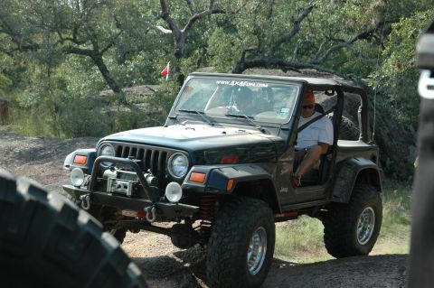 2001 Jeep Wrangler - A black 2001 Jeep Wrangler navigates a rocky trail, its off-road capabilities with a winch and oversized tires.