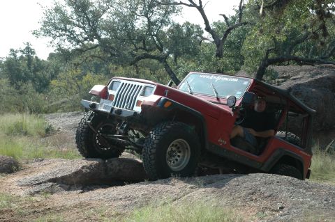 2001 Jeep Wrangler - Red Jeep Wrangler TJ navigating rocky terrain with a driver visible.