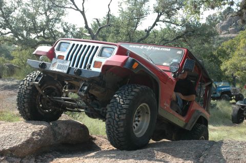 2001 Jeep Wrangler - Red Jeep Wrangler navigating rocky terrain with other vehicles present.